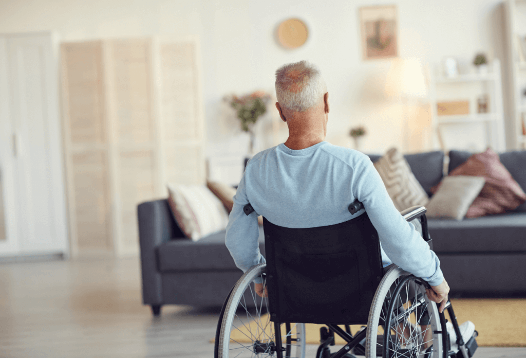 A picture of an older man from behind sitting in a wheelchair in his living room