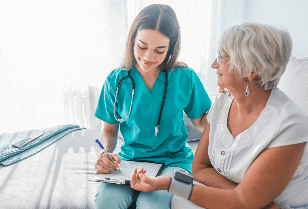 A doctor sitting next to an elderly woman patient and writing on a clipboard