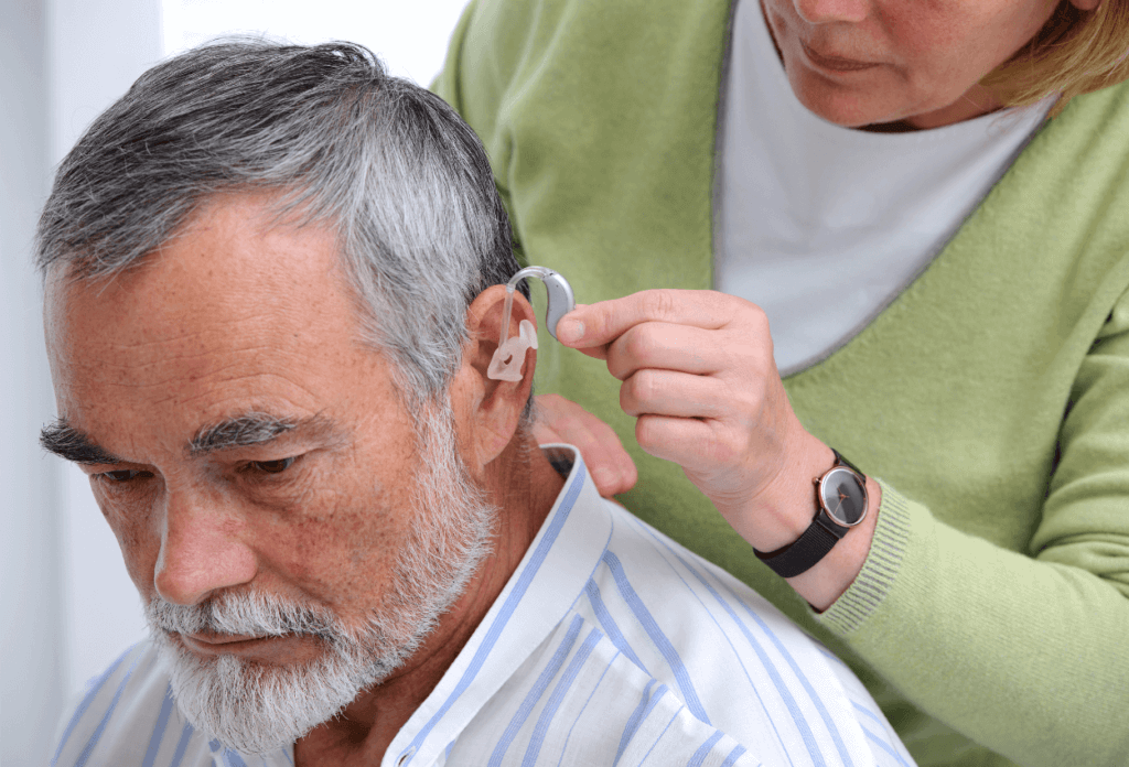 A woman putting hearing aids in the ear of an elderly man