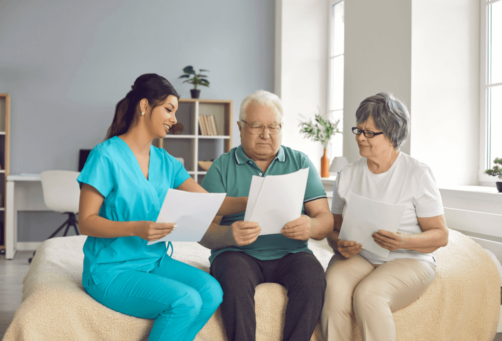 A healthcare provider in blue scrubs sitting with two elderly patients, holding papers and discussing them