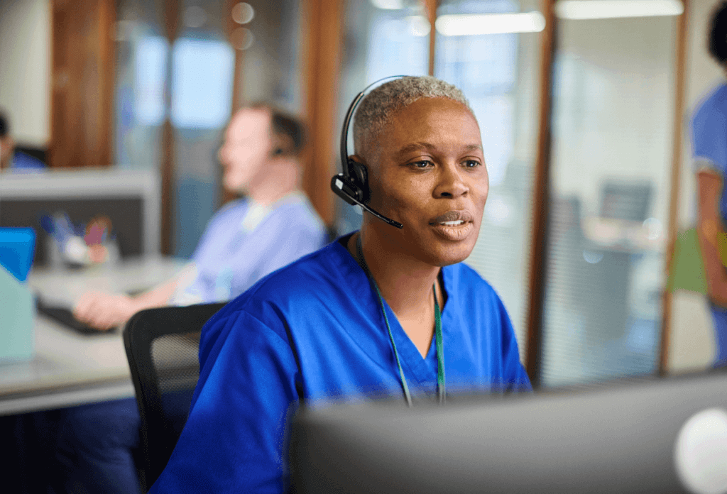 A healthcare professional in scrubs and a headset, working at a computer