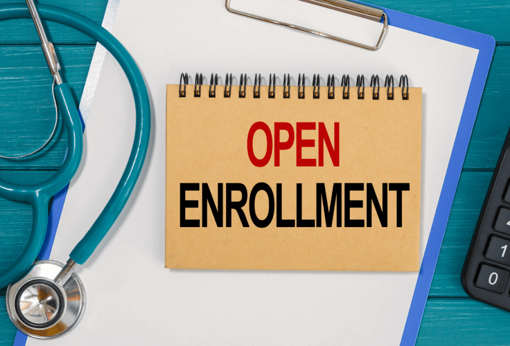 A close up of a stethoscope and a calculator with a notebook in the middle that says "open enrollment"