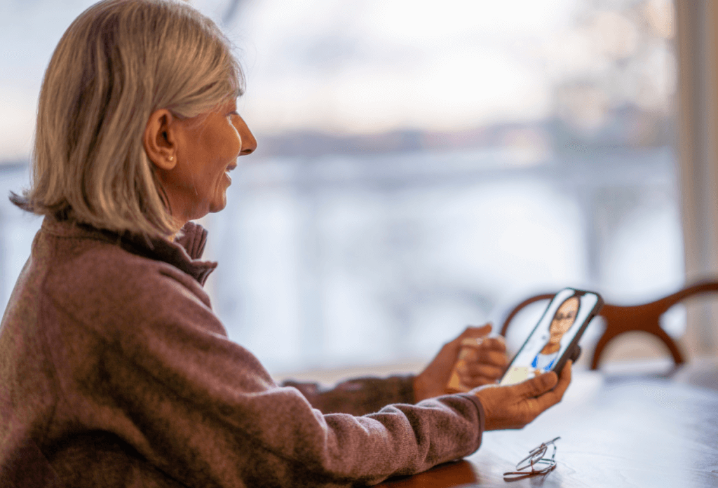 A picture of an older woman sitting at a table while on a virtual telehealth appointment.