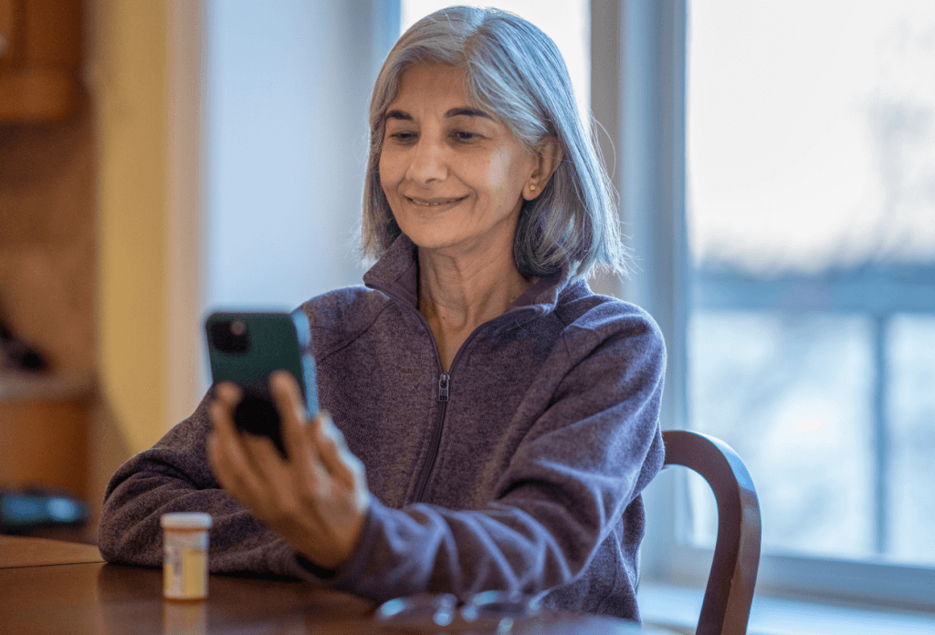An older woman holding her phone while sitting at a table with her medication.