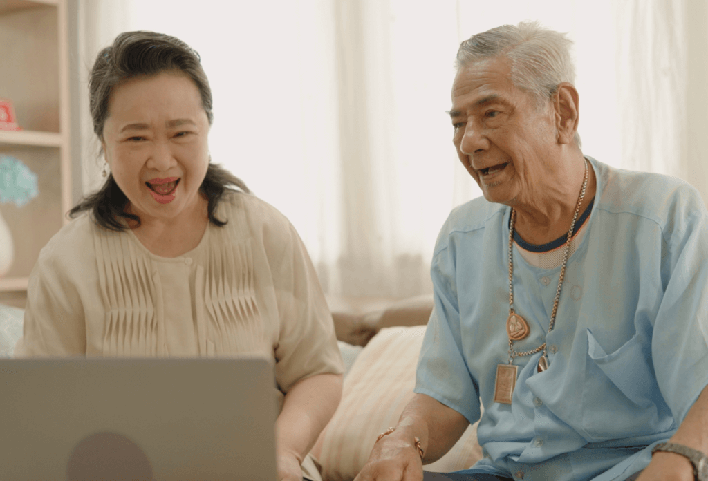 A picture of two individuals sitting at a computer on a telehealth appointment together while smiling.