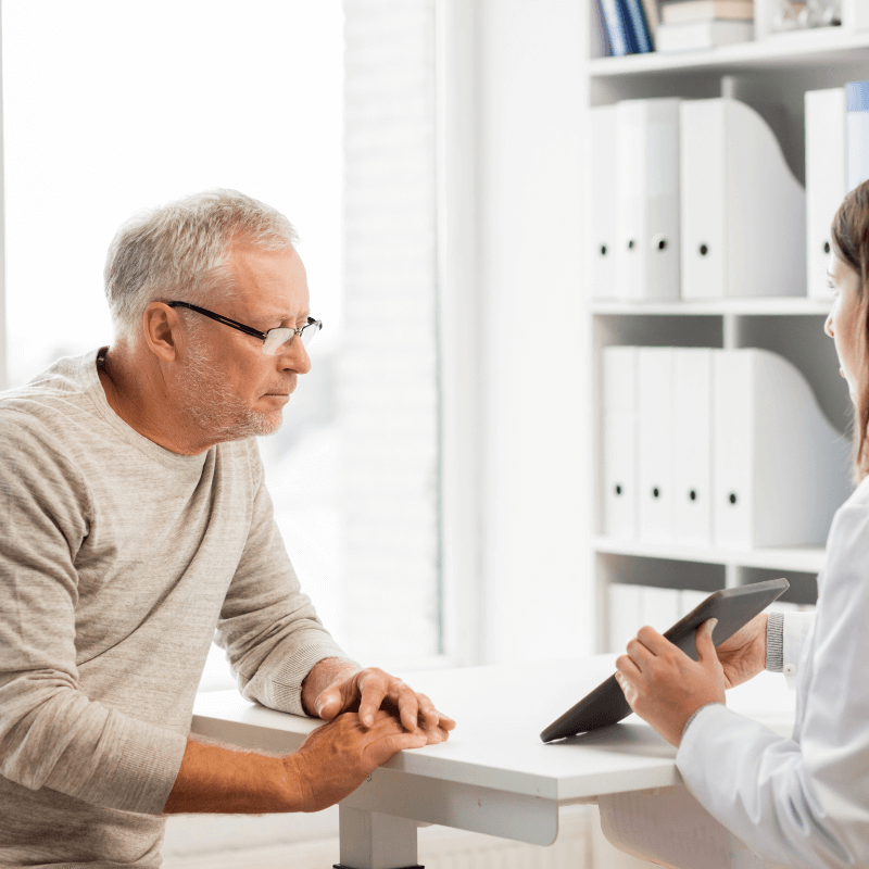 There's an older gentleman with glasses looking at an ipad screen with a woman wearing a white coat in an office.