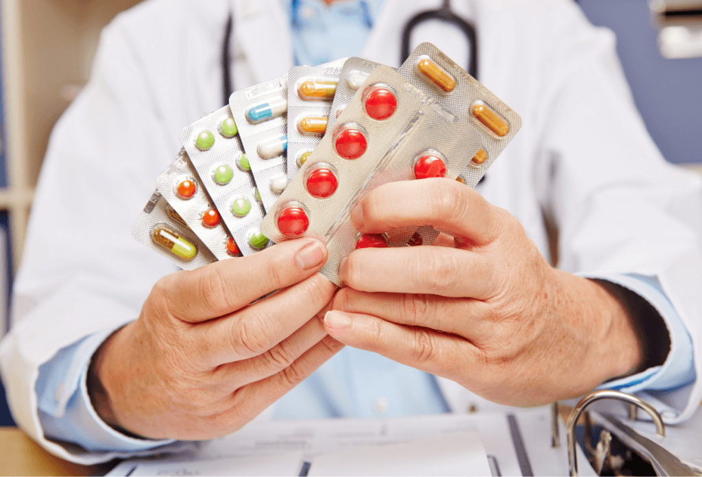 A doctor is holding a selection of prescription pill samples to share with a senior citizen.