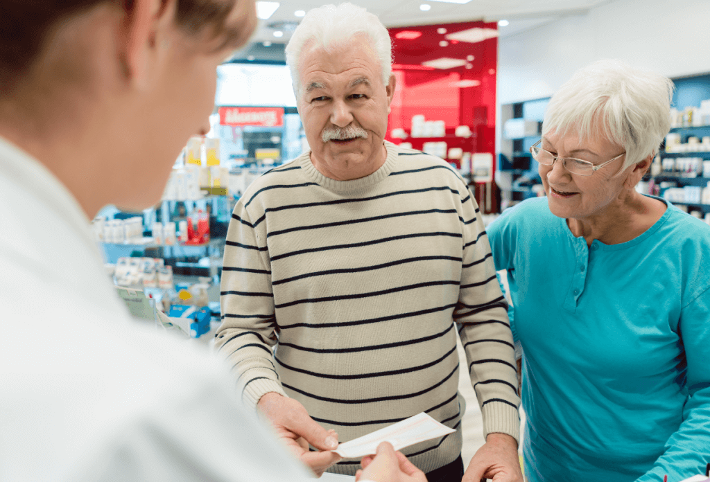 A male and a female senior citizen are smiling and speaking with a pharmacist about their prescription medications.