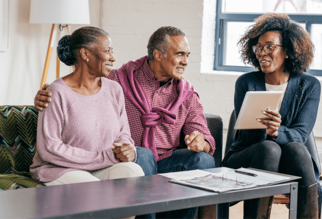 A senior citizen couple is listening to are seated listening to a female insurance agent help them learn more about not losing medicare eligibility.