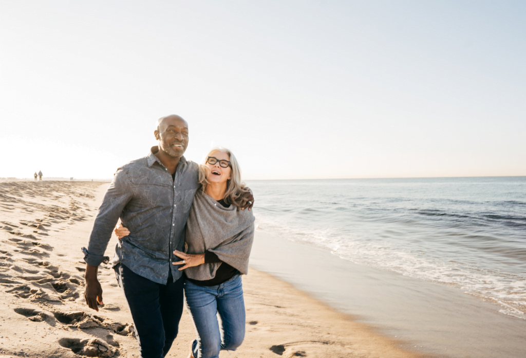 A senior citizen couple is walking on the beach in a blog about losing medicare eligibility.