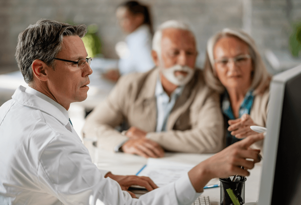 A senior citizen couple is looking at a computer screen with a doctor in a blog about losing medicare eligibility.