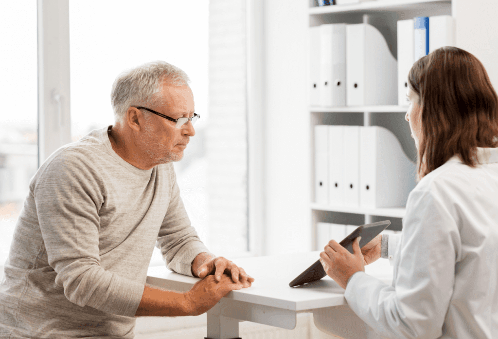 A male senior is meeting with a doctor holding an ipad in an image for a blog titled "Medicare Open Enrollment 2024-2025: Your Guide to Making the Right Choice."
