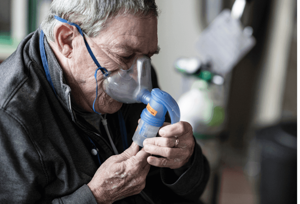 A male senior is breathing into a COPD machine in a blog image related to Medicare and chronic illness.