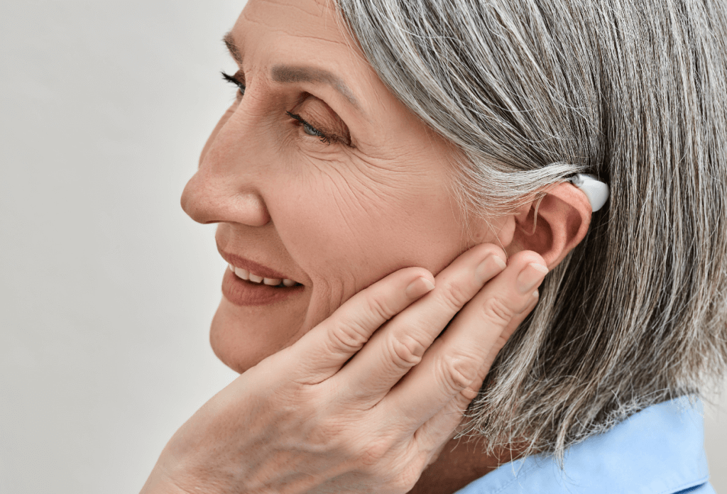 A picture of a senior woman holding her ear with a hearing aid on her ear.
