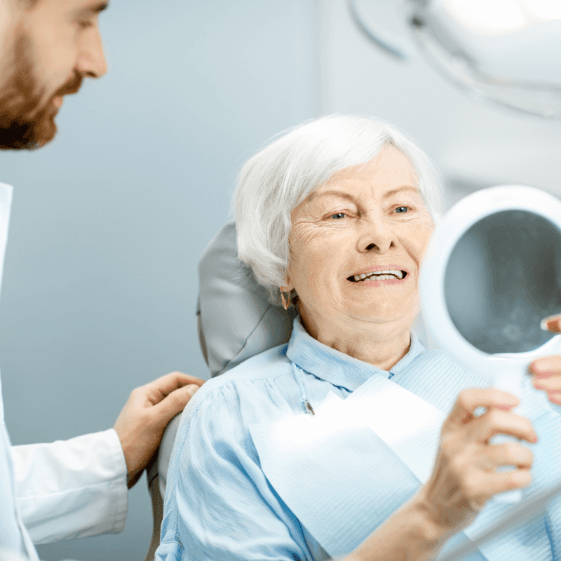 A picture of a senior woman looking into a mirror after having dental implants installed.
