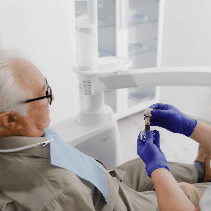 A picture of a senior man talking to his dentist about his implants. His dentist is showing him how the dental implants work.