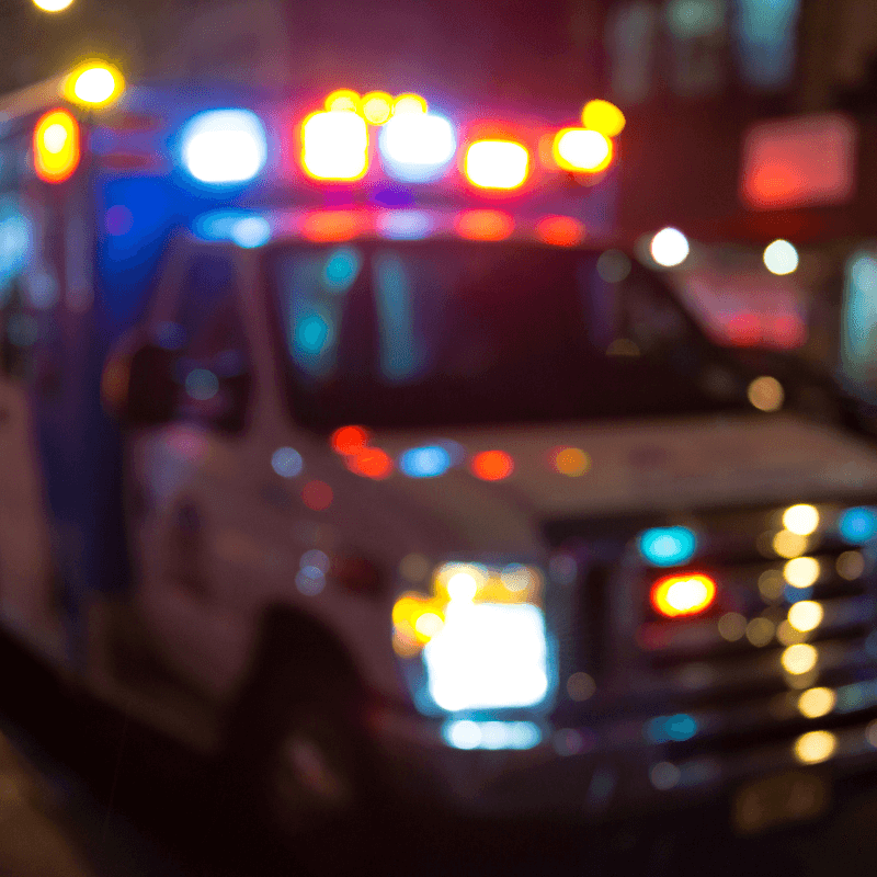 A blurry picture of an ambulance with their lights on.