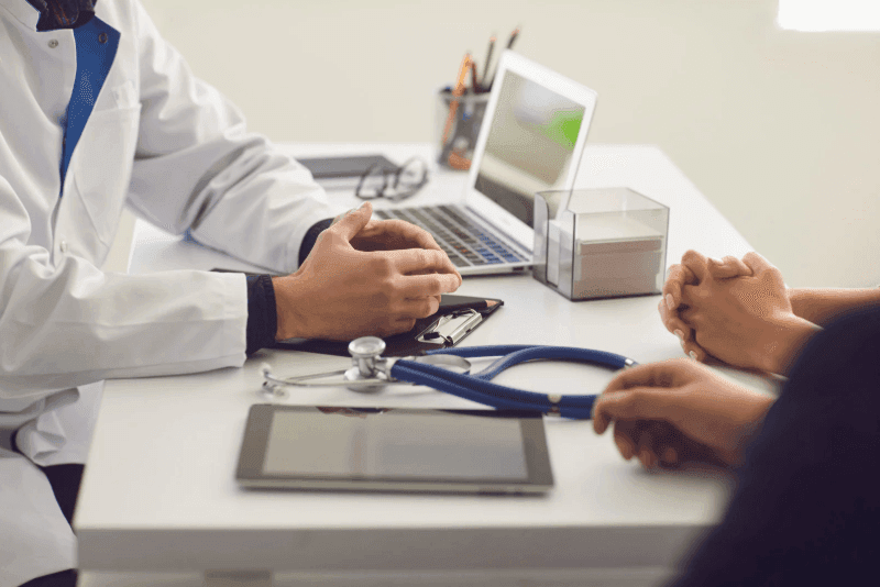 Doctor consulting with patients at a desk with a stethoscope and a laptop.
